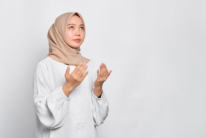 Calm Muslim woman in headscarf and light blouse looking up in prayer