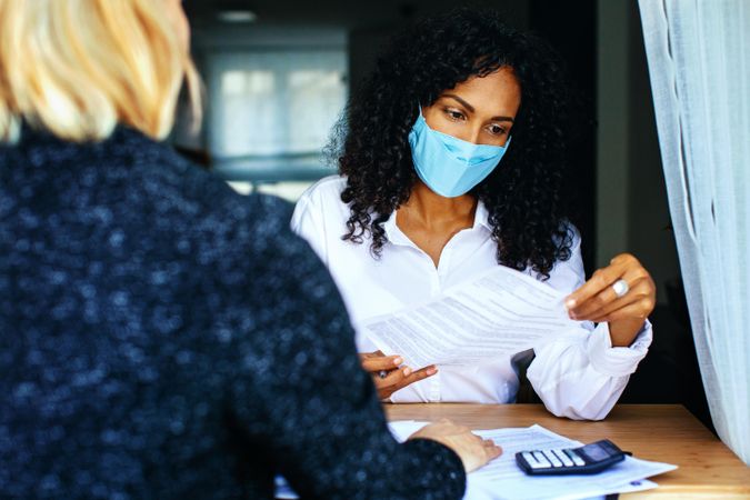 Woman with colleague reading documents at a work meeting while wearing a facemask