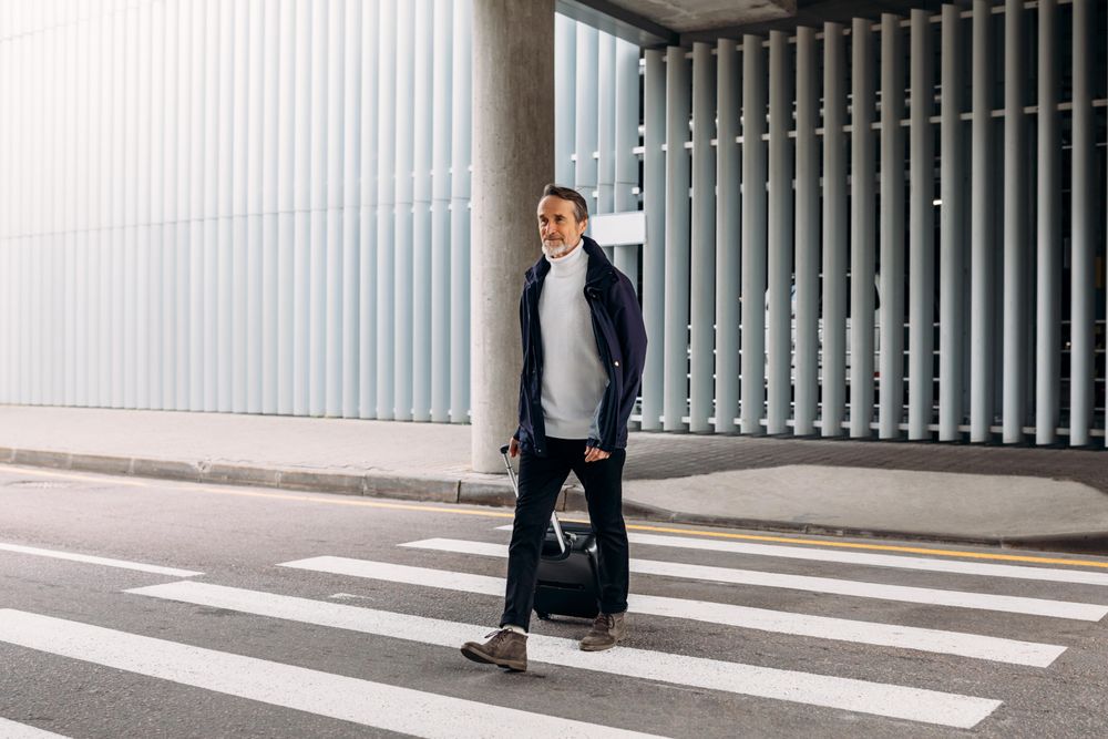 Man with suitcase crossing the street outside of airport