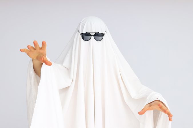 Concept of Halloween, woman in ghost costume and sunglasses on light background