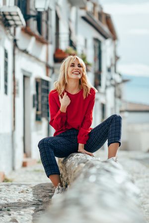 Happy blonde female with red shirt sitting outdoors, vertical