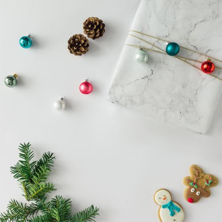 Christmas layout made of marble wrapped present, baubles, cookies, pinecones on light background