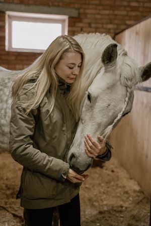 Woman hugging horse with long mane in face in stable