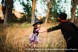 Little girl in witch costume reaching out to her brother in the forest 567ze4