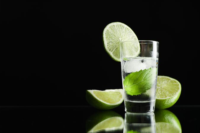 Tequila shot with lime, mint and ice against dark background