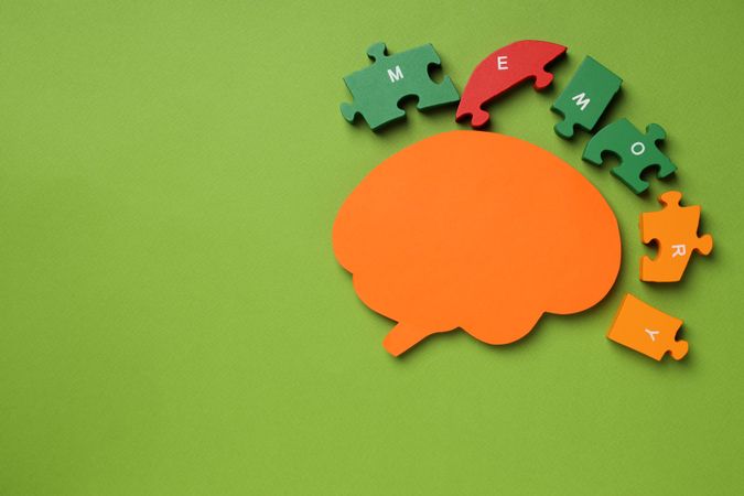 Paper cut out of brain with puzzle pieces on green background, copy space