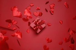 Red box with red bow on red background surrounded by falling red hearts