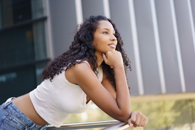 A young woman leans on a railing outdoors, reflecting on life while enjoying natures beauty