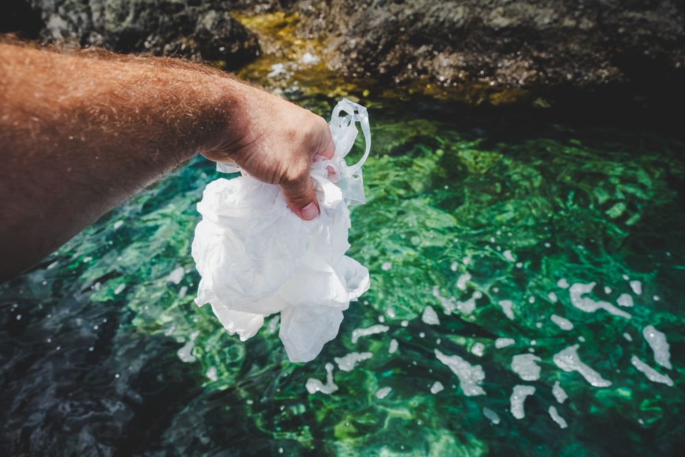 Crop man pulling plastic bag out of water