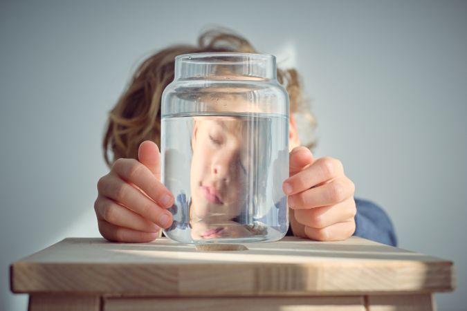 Sleepy boy reflection in glass jar with water