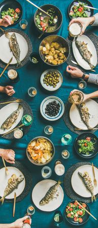 Flat-lay of human hands, beer glasses, grilled sea bass, narrow composition