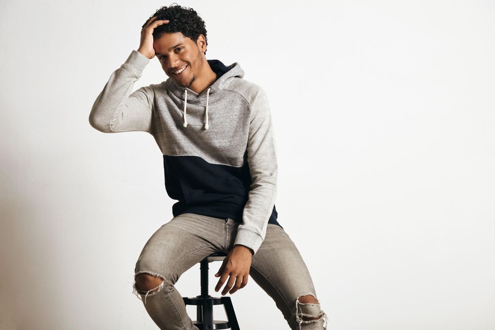 Man holding head while smiling and sitting on stool in studio shoot