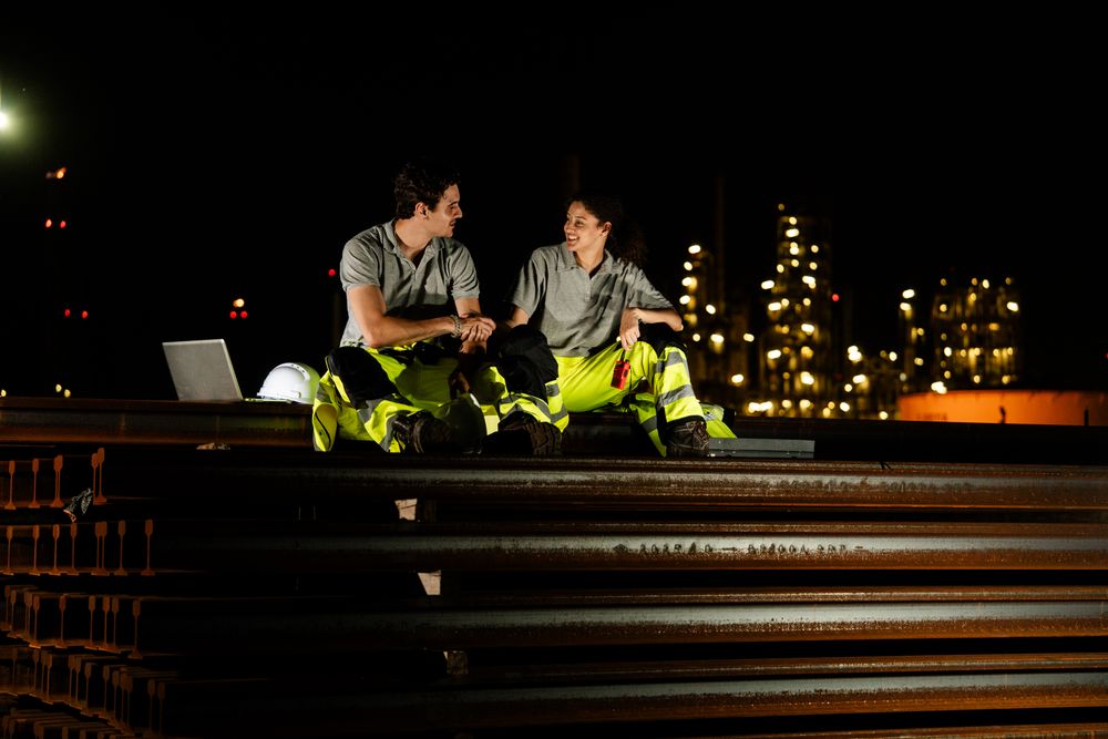 Engineer team sit for taking a break, talking with colleauge at night. Refinery worker at oil factory, working overtime, petroleum chemical industry, after work resting time