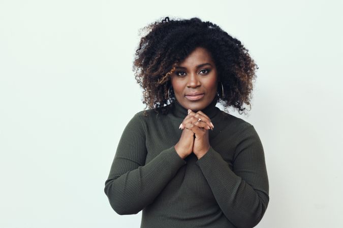 Portrait of serious Black woman in green turtleneck holding her hands together
