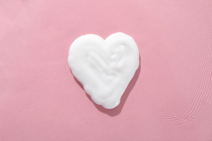 Hand cream in the shape of a heart, close-up, on a pink background.
