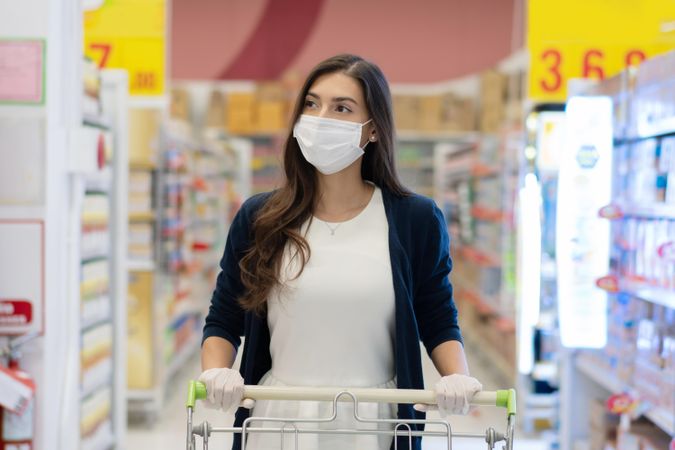 Woman in surgical mask pushing grocery cart down the aisle