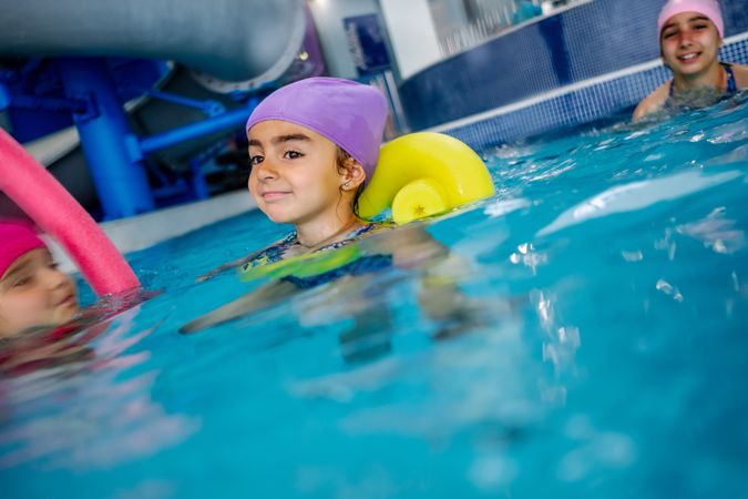 Cheerful girl in hat smiling and swimming in pool in water park