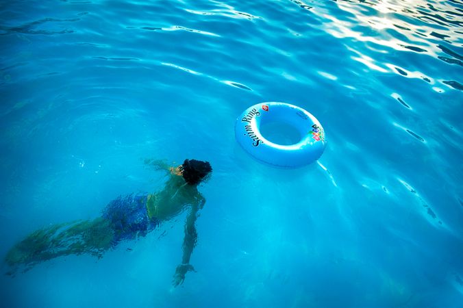 Person swimming underwater near inflatable ring in swimming pool