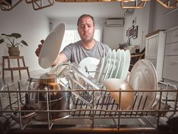 Puzzled man unloading dishwasher in kitchen
