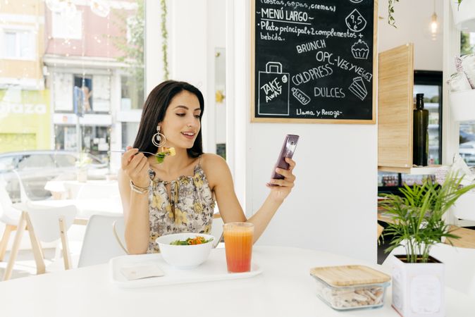 Cheerful woman with healthy food browsing smartphone in cafe