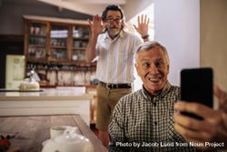 Funny man taking selfie with friend standing at back making hand gestures 4dA8lb