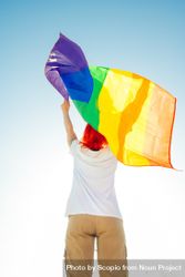 Back view of a person holding rainbow flag under blue sky 49pG65