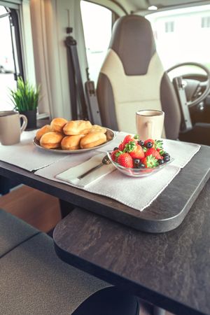 Breakfast pastries, coffee and bowl of berries in camper van, vertical