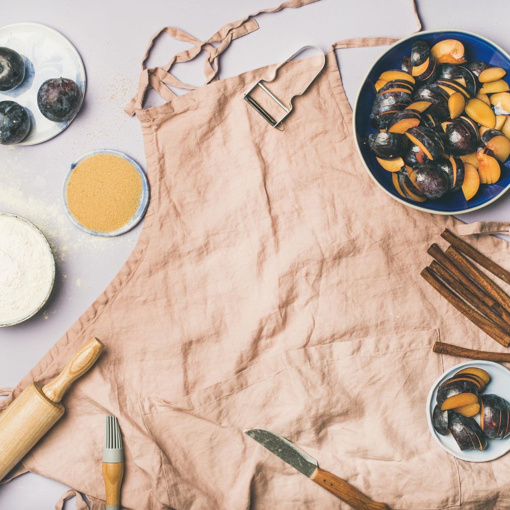 Baking ingredients and tools, plums, pastry brush, cinnamon, eggs on pink apron, square crop