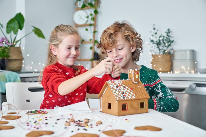Delighted children making gingerbread house in kitchen