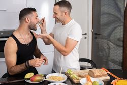 Male couple tasting pasta as they prepare meal