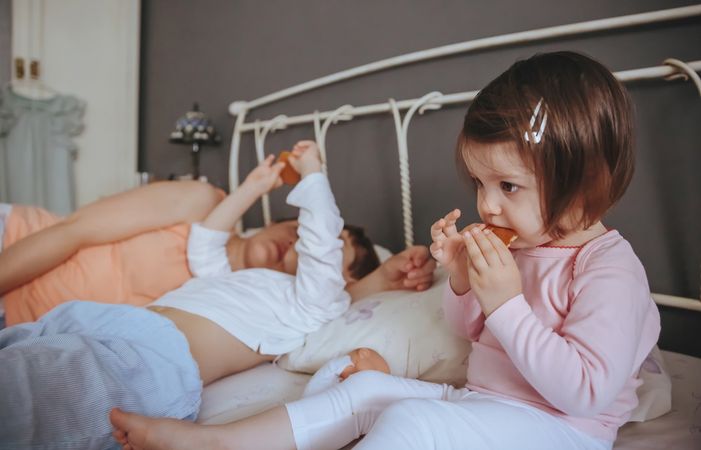 Portrait of content little girl eating cookies in bed next to her mother and brother