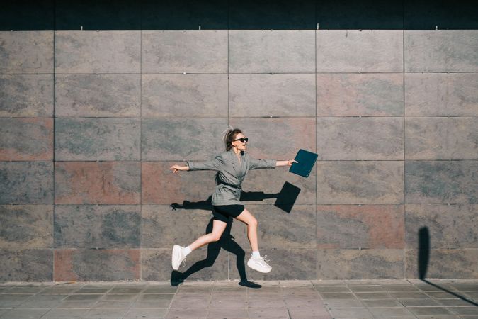 Woman joyfully jumping along wall with tablet