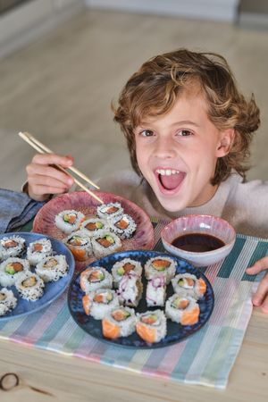 Cheerful boy eating sushi in kitchen