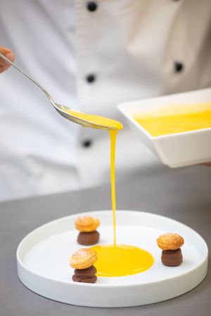 Chef decorating confectionery mushrooms with yellow syrup in plate