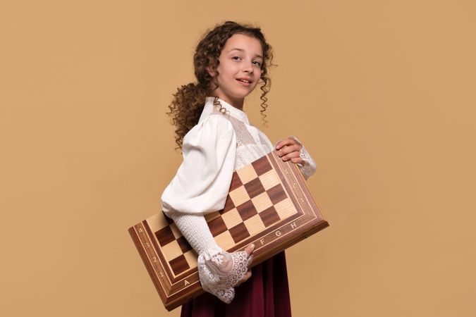 Young girl proudly carrying large wooden chessboard
