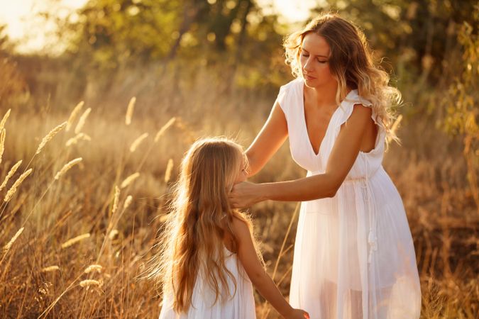 Woman fixing a little girls long hair in marsh at sunset