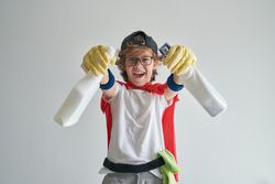 Joyful boy in housekeeper costume standing with detergent bottle