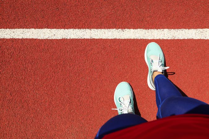 Female legs in sneakers on red athletic track background, space for text