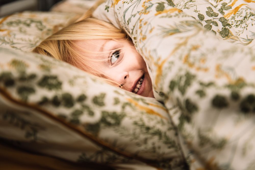 Blond child peeking over a blanket