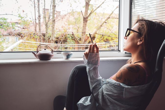 Woman relaxing with tea pot and spliff by the window