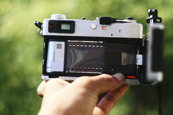 Hand holding camera with open back showing film