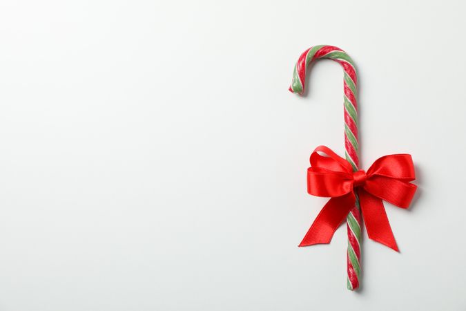 Sweet candy cane with bow on studio background, space for text