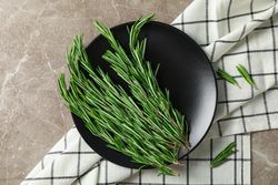 Plate with rosemary and towel on grey table, top view