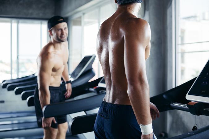 Two men talking while standing on treadmill in gym