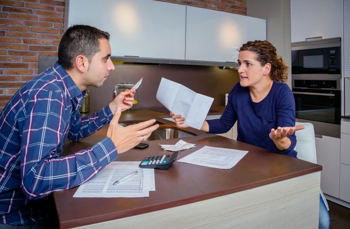 Man holding up credit cards and arguing with woman over bills