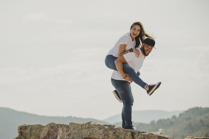 Lovely man holding woman on back at mountain cliff
