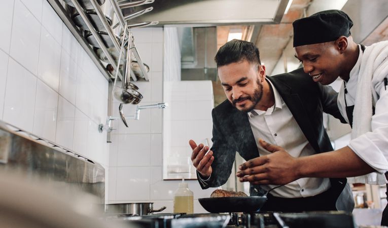 Manager smelling the aroma of dish cooking on stove with chef