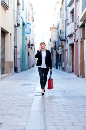 Woman wearing a blazer and speaking on phone while walking down street