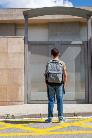 Back of boy in backpack standing in front of the school doors