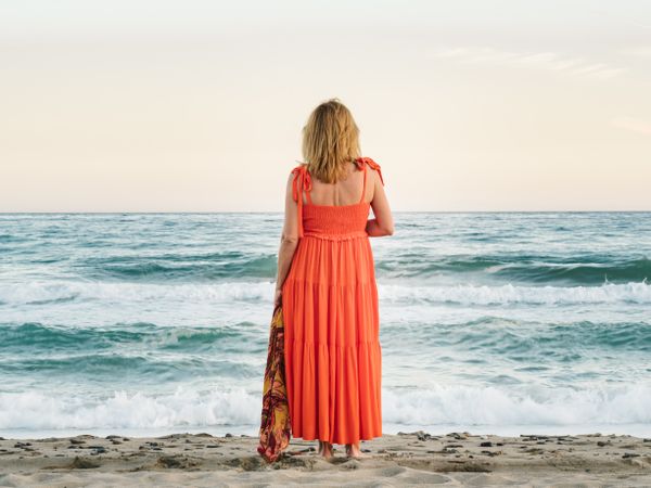 Woman in red dress looking along at seaside
